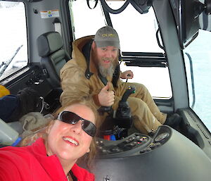 Two people inside the cabin of a snow groomer