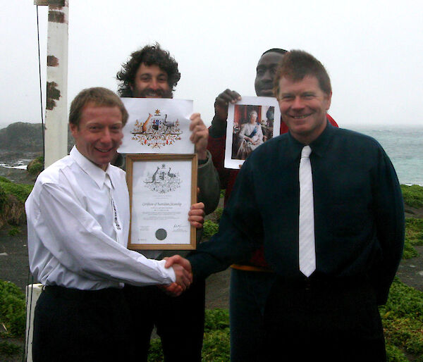 Andy Wakefield proudly holding his Citizenship Certificate at the completion of the conferral ceremony with Graeme Beech (Station Leader and Presiding Officer), Luke Gadd (Ranger), and Segun Adewumi (Met Bureau Technician) in the background.