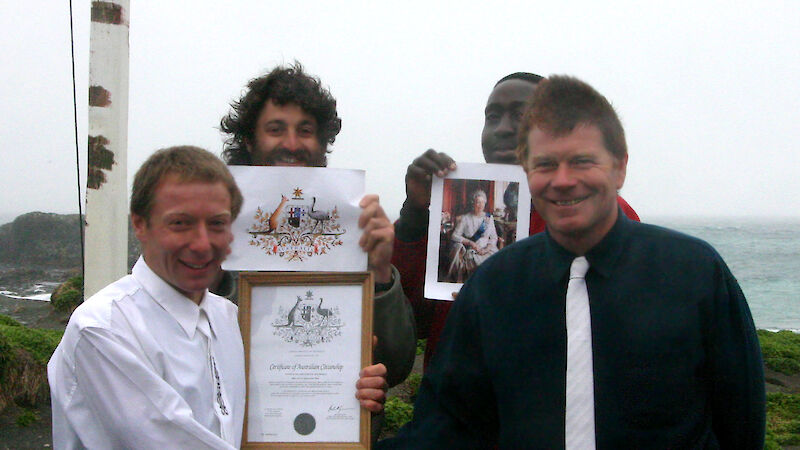 Andy Wakefield proudly holding his Citizenship Certificate at the completion of the conferral ceremony with Graeme Beech (Station Leader and Presiding Officer), Luke Gadd (Ranger), and Segun Adewumi (Met Bureau Technician) in the background.