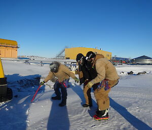 Three expeditioners carefully walking toward a blue Hägglunds