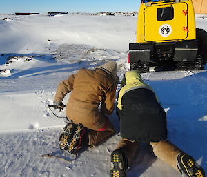 Two expeditioners on their hands and knees in the snow make their way to a vehicle