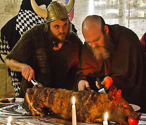 Two people dressed as a viking and a brother carving a BBQ pig