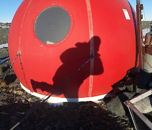 Persons shadow on the side of a small round red hut