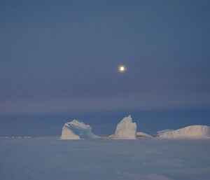 Full moon in the background above ice bergs and sea ice