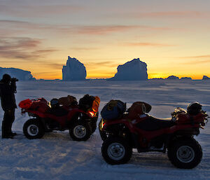 Two quad bikes and an expeditioner on the sea ice, stunning yellow sunset in the background