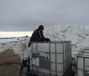 Expeditioner standing over a large white container used for storing waste water