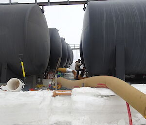 Expeditioner standing in the middle of 12 large fuel tanks with hose blowing heat linked to one of the tanksto one of t