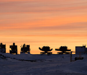 Five large vehicles with a bright orange and yellow sunset