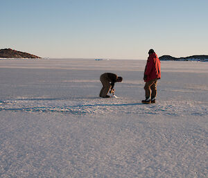Two expeditioners on very smooth sea ice drilling a hole through the ice