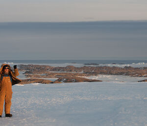 Expeditioner standing on an icy plateau sea ice and islands far into the background