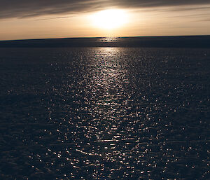 Low dark cloud with sun also sitting low, sun reflecting on the sea ice