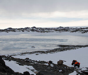 Two quad bikes parked up at base of hill open water in sections of a frozen fjord