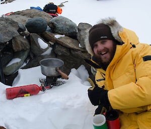 Expeditioner sitting amongst snow and rock with a camping stove