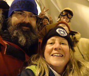 Two expeditioners posing for a photo with a few people in the background joining in