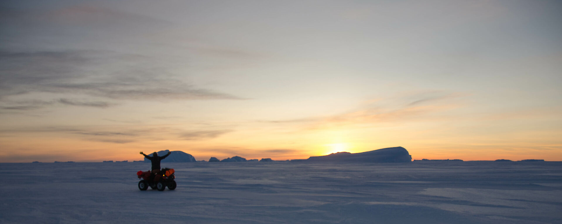 Quad bike rider with icebergs and a sunset in the background