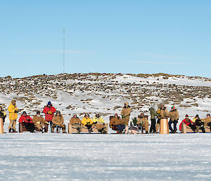 The 2014 winter team expeditioners sit on lounges, in a line on the sea ice
