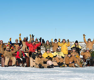 The 2014 winter expeditioners sit on lounges on the sea ice, many cheering with their arms raised
