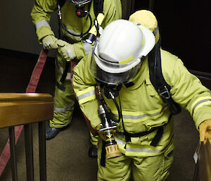 Two expeditioners in firefighting gear carry a hose together during a training exercise