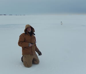 Expeditioner kneeling on the sea ice with Adélie penguin in the background