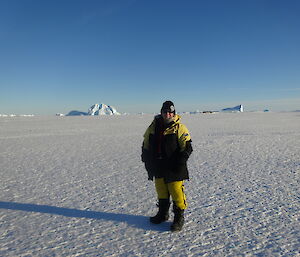 Expeditioner standing on sea ice, with icebergs in the background