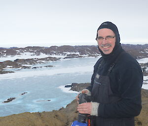 Expeditioner on top of a rocky hill looking down over the sea ice