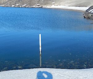 A person’s shadow pointing to a measuring stick in a lake