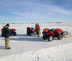 Two expeditioners and three quad bikes on the sea ice, expeditioner surveying the skiway