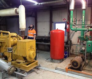 Expeditioner inside the power house standing near a large yellow generator