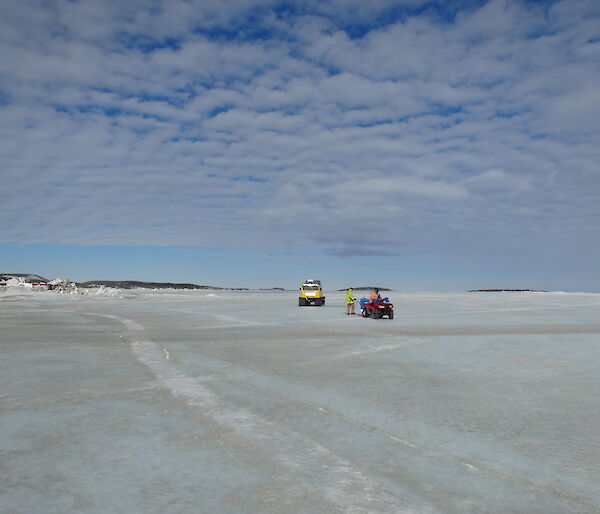 Yellow Hägglunds parked up on the sea ice with a team of 2 attending to it