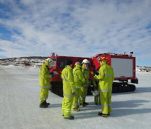 Expeditioners dressed in fire clothing listening to the fire chief