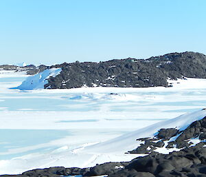 Small green hut on top of a black rocky hill in the distance