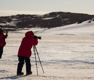 Two expeditioners wearing red jackets photographing seals