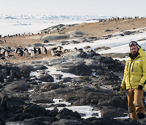 Expeditioner wearing bright yellow jacket with nesting adelie penguins in the background