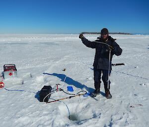 Expeditioner on the sea ice holding a cable over a hole in the sea ice