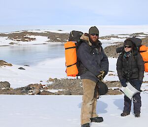 Two expeditioners with backpacks and a frozen lake in the background