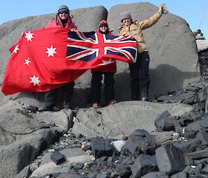 Three expeditioners holding up a flag