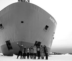 Eight expeditioners on the sea ice with the Aurora Australis in the background