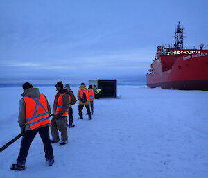 Group of people dragging the hose back into a container alongside the Aurora Australis