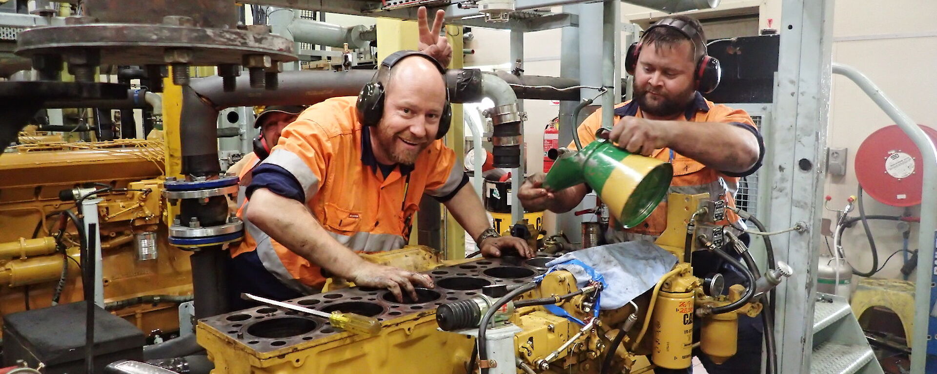 Two diesel mechanics grinning over an engine in the workshop at Davis