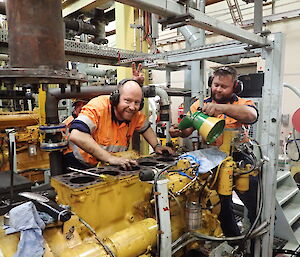 Two diesel mechanics grinning over an engine in the workshop at Davis