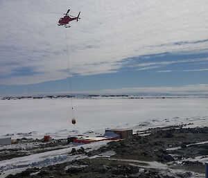 Helicopter flying off camera carrying a water bladder towards the sea ice on a sling
