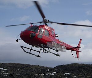 red helicopter with a fitted cargo cage landing with a background of rocky landscape