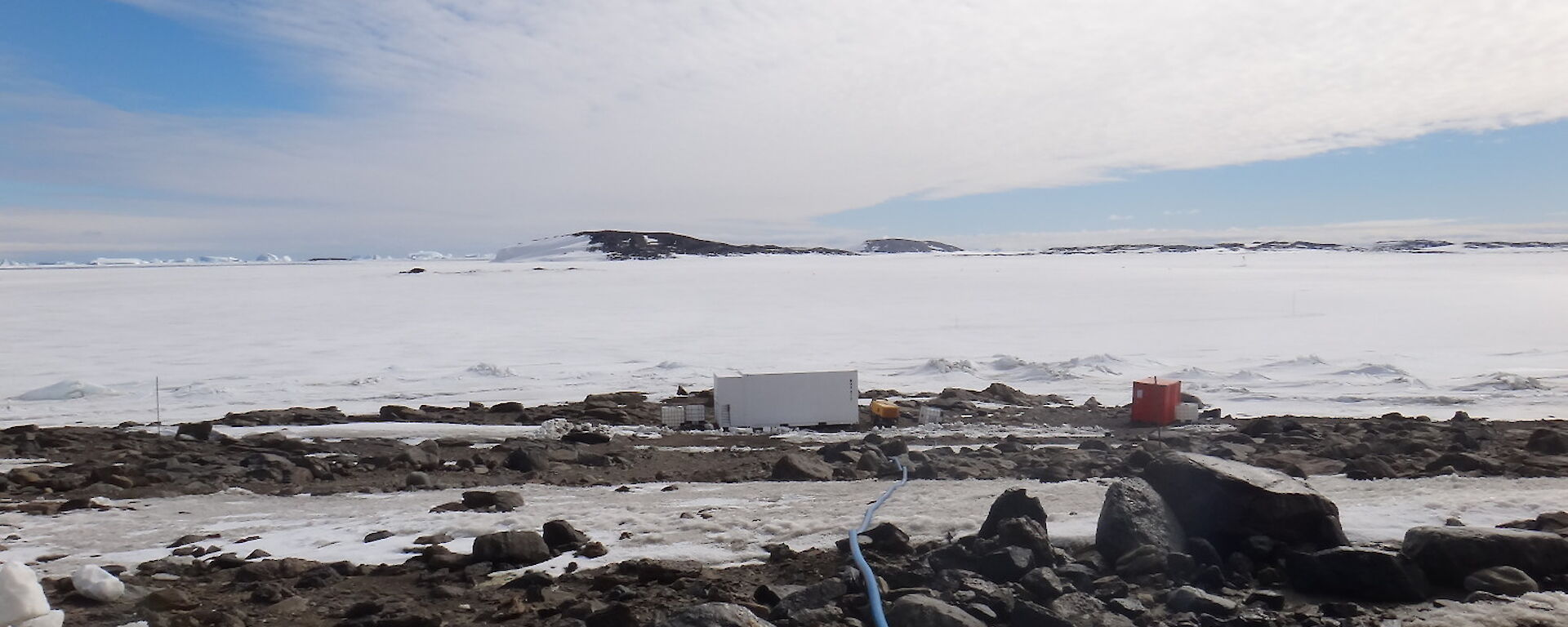 Blue pipe running down to a small white container hut beside the sea ice where known as the minicosm