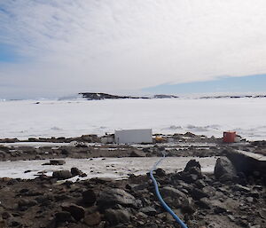 Blue pipe running down to a small white container hut beside the sea ice where known as the minicosm