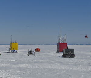 A series of multicoloured prefabricated huts on the plateau at landing site. Helicopter taking off