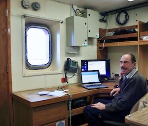 Man sitting at a desk in the Bureau of Meteorology cabin on the Aurora Australis