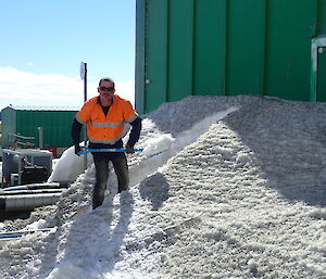 Tradesperson standing in front of a green building staring at the camera, shovelling snow.