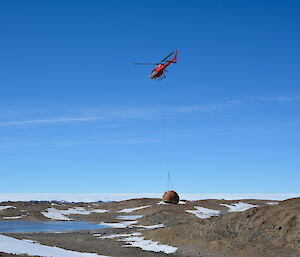Helicopter carrying the old hut by a sling in mid flight