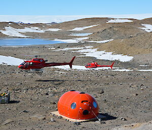 Two red helicopters in background with new hut in foreground