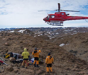 Helicopter in hover in background above expeditioners standing on ridgeline in foreground